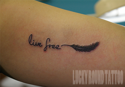 羽とlive freeの筆記体のタトゥー Lucky Round Tattoo